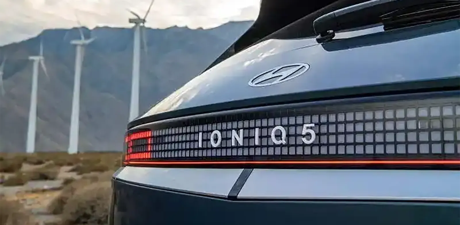 Hyundai Ioniq 5 parked near a wind farm, symbolizing eco-friendliness.