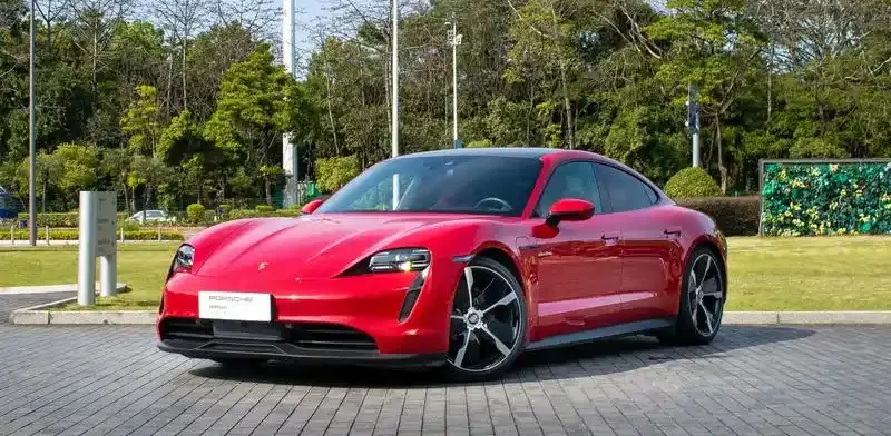 How to Charge Porsche Taycan: Red Porsche Taycan parked beside a tree-lined road, showcasing its design and charging capability
