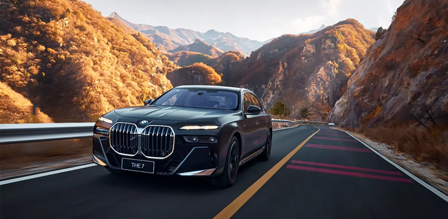 how to charge bmw i7 a complete guide: A black BMW i7 driving on an asphalt road with golden autumn trees and mountains in the background.