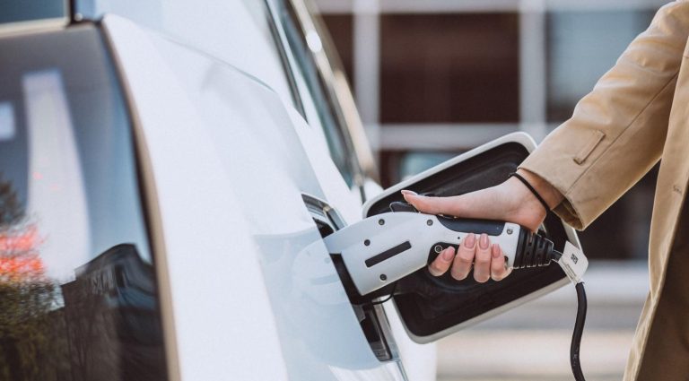 Hand plugging a 40 amp level 1 and 2 portable EV charger into a white electric car