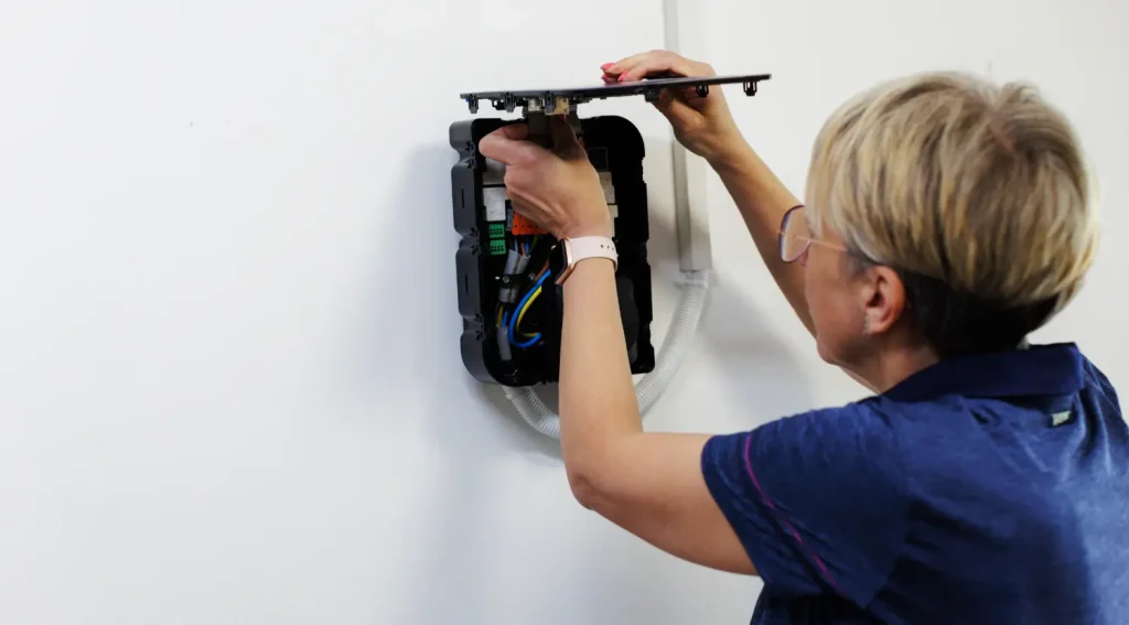 after acquiring ev charger permit, Woman checking internal wiring of a wall-mounted EV charger
