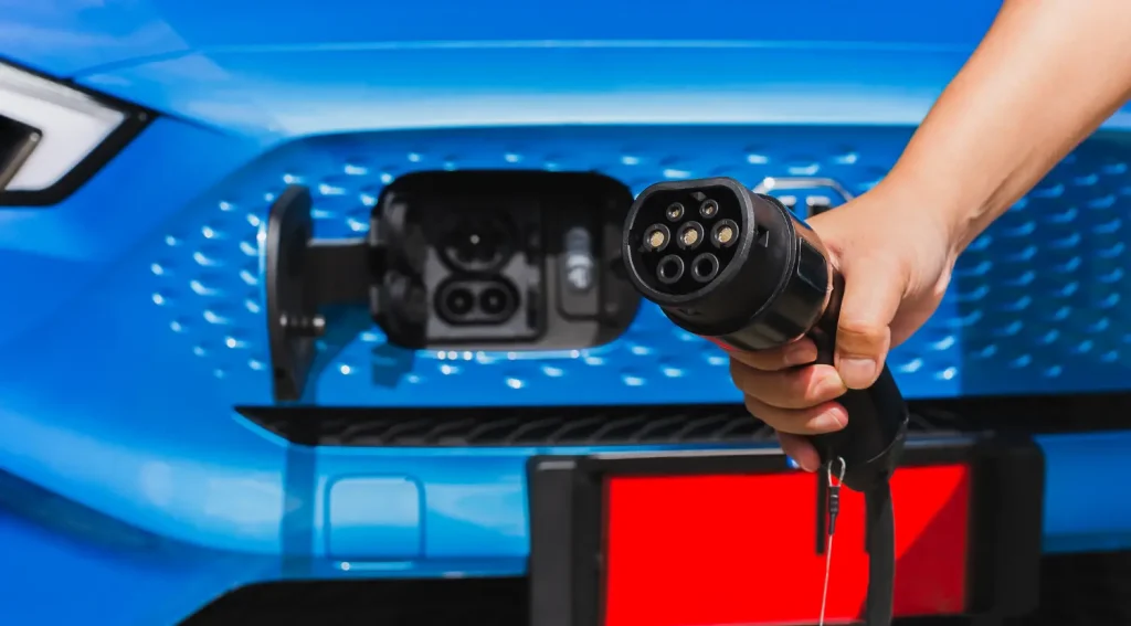 Close-up of an EV connector plug being held near a vehicle charging port