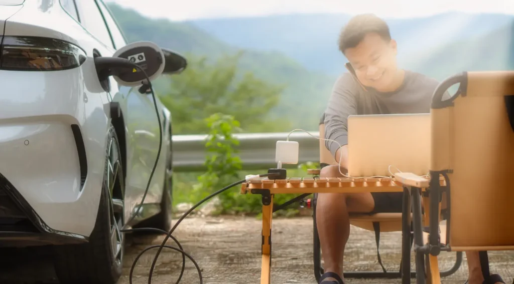 Man using laptop powered by electric car through Vehicle-to-Load (V2L) connection outdoors