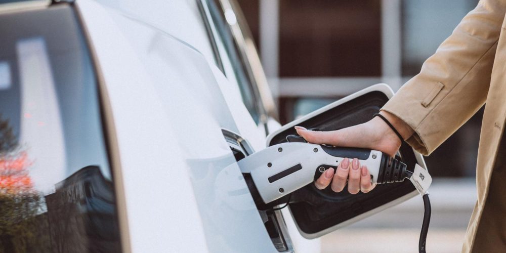 Hand plugging a 40 amp level 1 and 2 portable EV charger into a white electric car