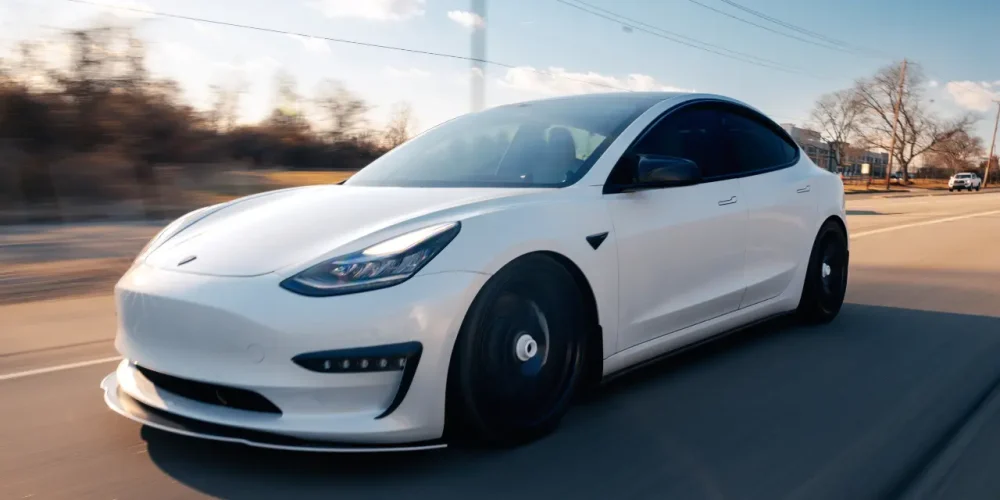 White Tesla driving on the road illustrating real-world Tesla battery lifespan