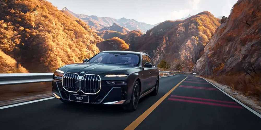 how to charge bmw i7 a complete guide: A black BMW i7 driving on an asphalt road with golden autumn trees and mountains in the background.
