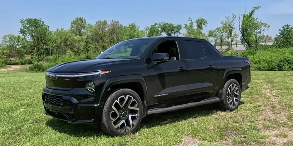 How to Charge Silverado EV: A black Silverado EV parked on a green grassy field with a forest in the background.