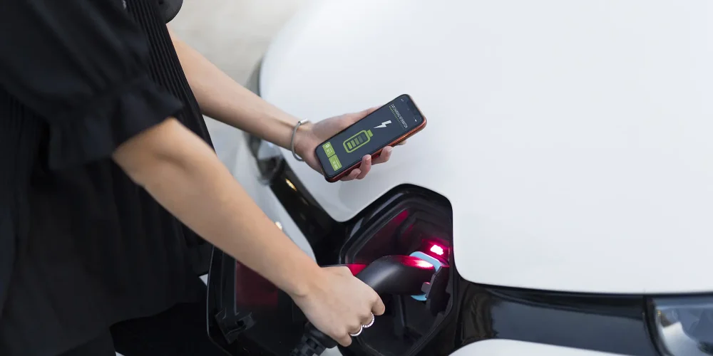 Person plugging in smart EV charger while using smartphone app to monitor charging session